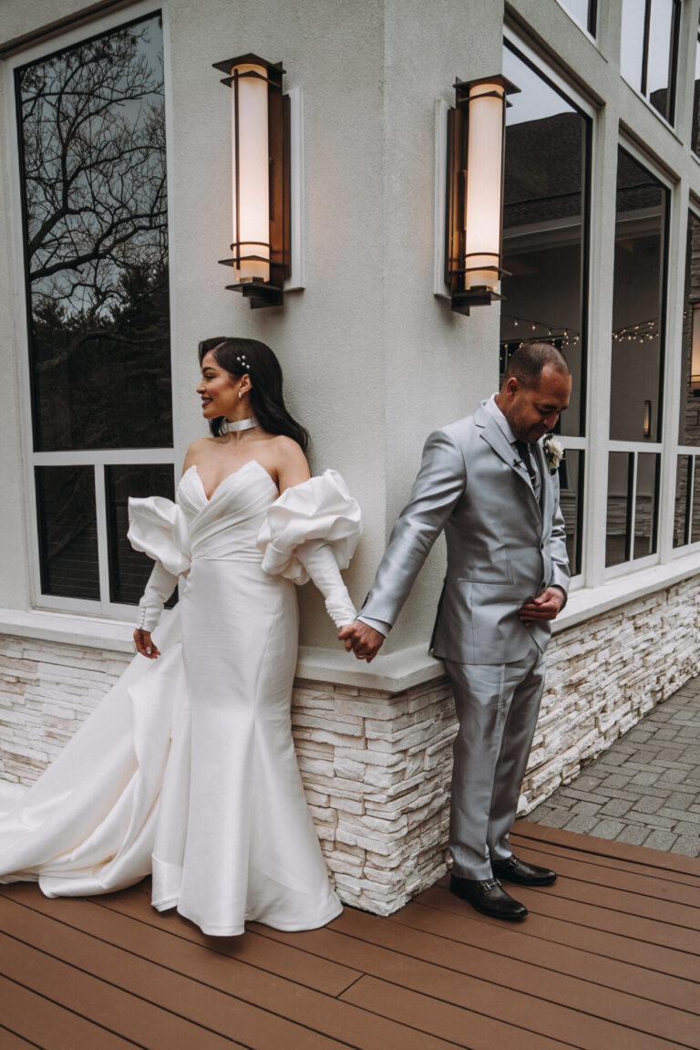 Bride and groom walking hand in hand along the outdoor terrace at Lakeview Pavilion in Foxborough, Massachusetts, showcasing modern architecture and elegant wedding portrait locations.