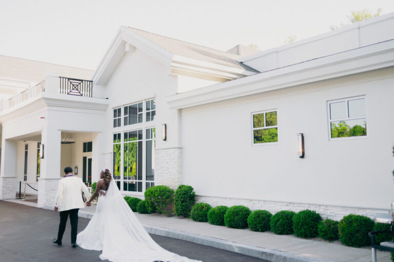 Bride and groom walking toward the entrance of Lakeview Pavilion in Foxborough, Massachusetts, showcasing the venue's modern white exterior and elegant wedding venue architecture.