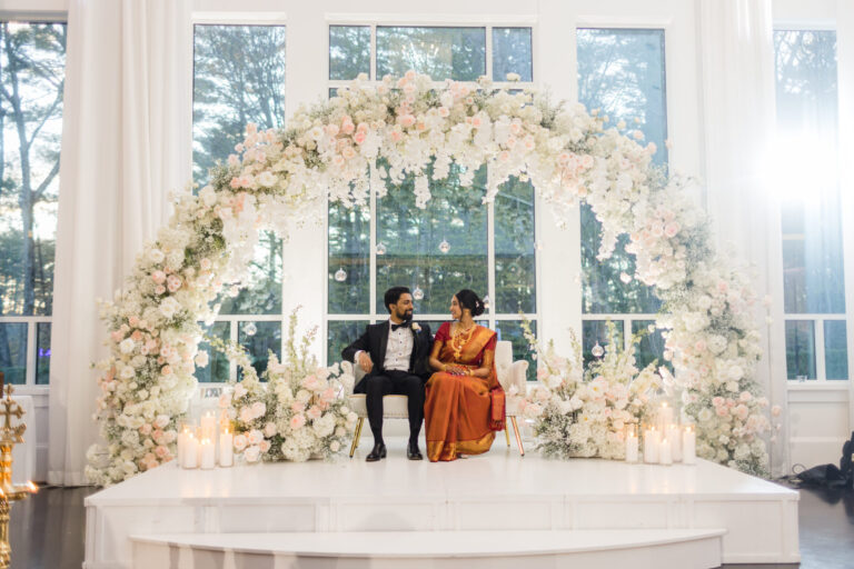 Couple seated beneath a stunning floral ceremony arch in the Lakeview Ballroom at Lakeview Pavilion in Foxborough, Massachusetts.