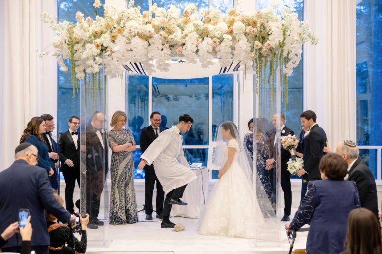 Couple participating in the breaking of the glass ceremony beneath a floral Chuppah in the Lakeview Ballroom at Lakeview Pavilion in Foxborough, Massachusetts.