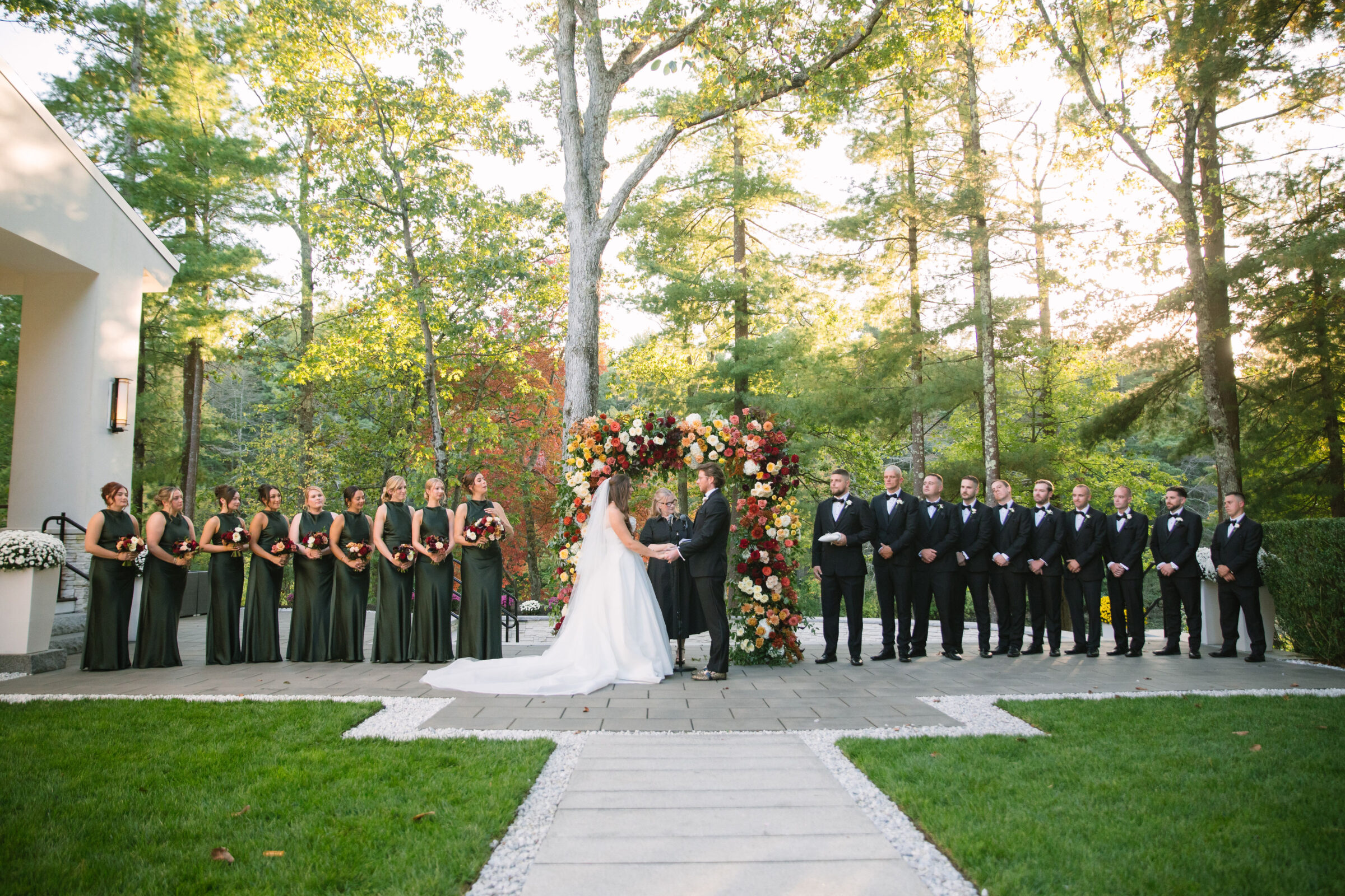 Bride and groom exchanging vows during a fall outdoor wedding ceremony at Lakeview Pavilion in Foxborough, Massachusetts beneath a colorful floral arch