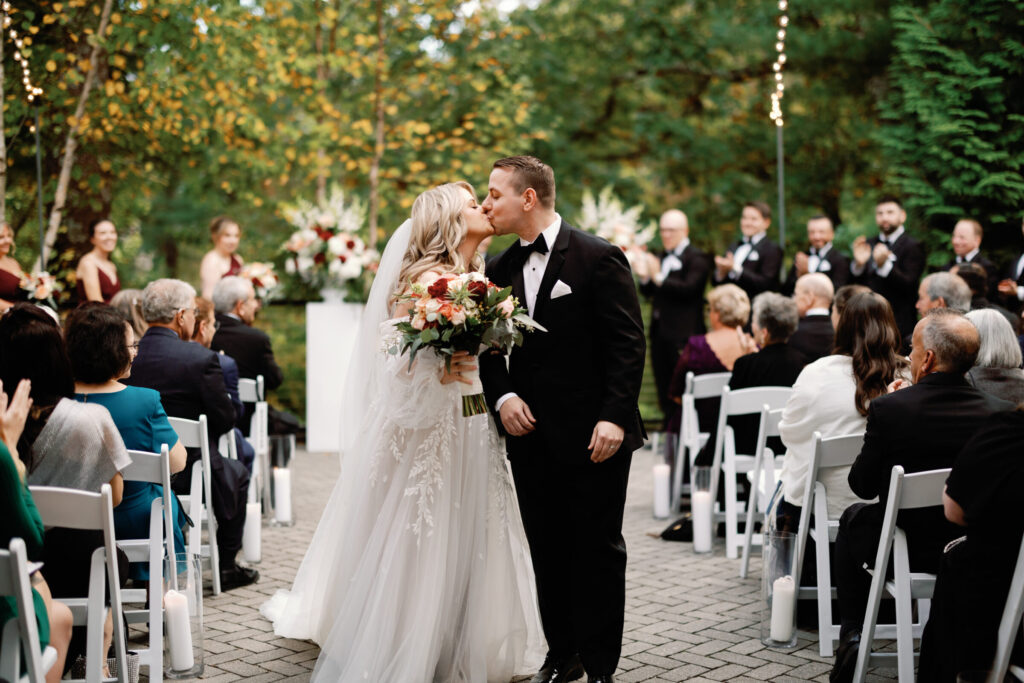 Bride and groom share their first kiss during an outdoor wedding ceremony on the private terrace outside the Lakeside Ballroom at Lakeview Pavilion in Foxborough, Massachusetts.