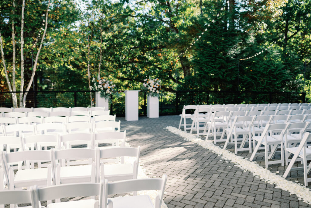 Outdoor wedding ceremony on the terrace at Lakeview Pavilion featuring white ceremony chairs, a romantic floral aisle, and a private wooded setting in Foxborough, Massachusetts.